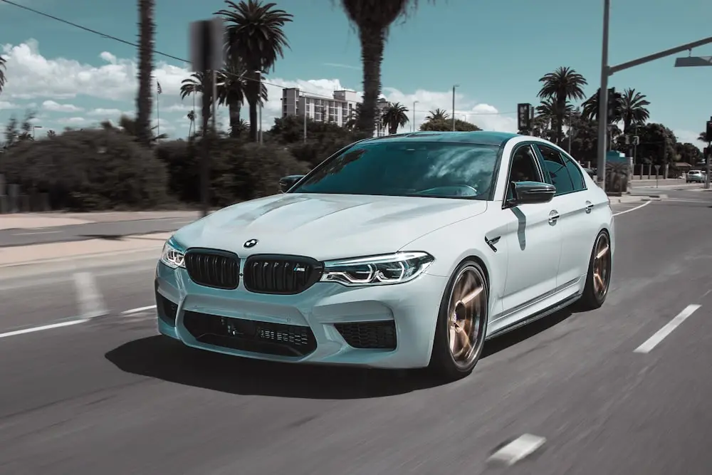White BMW M5 with flawless finish driving on a palm-lined street