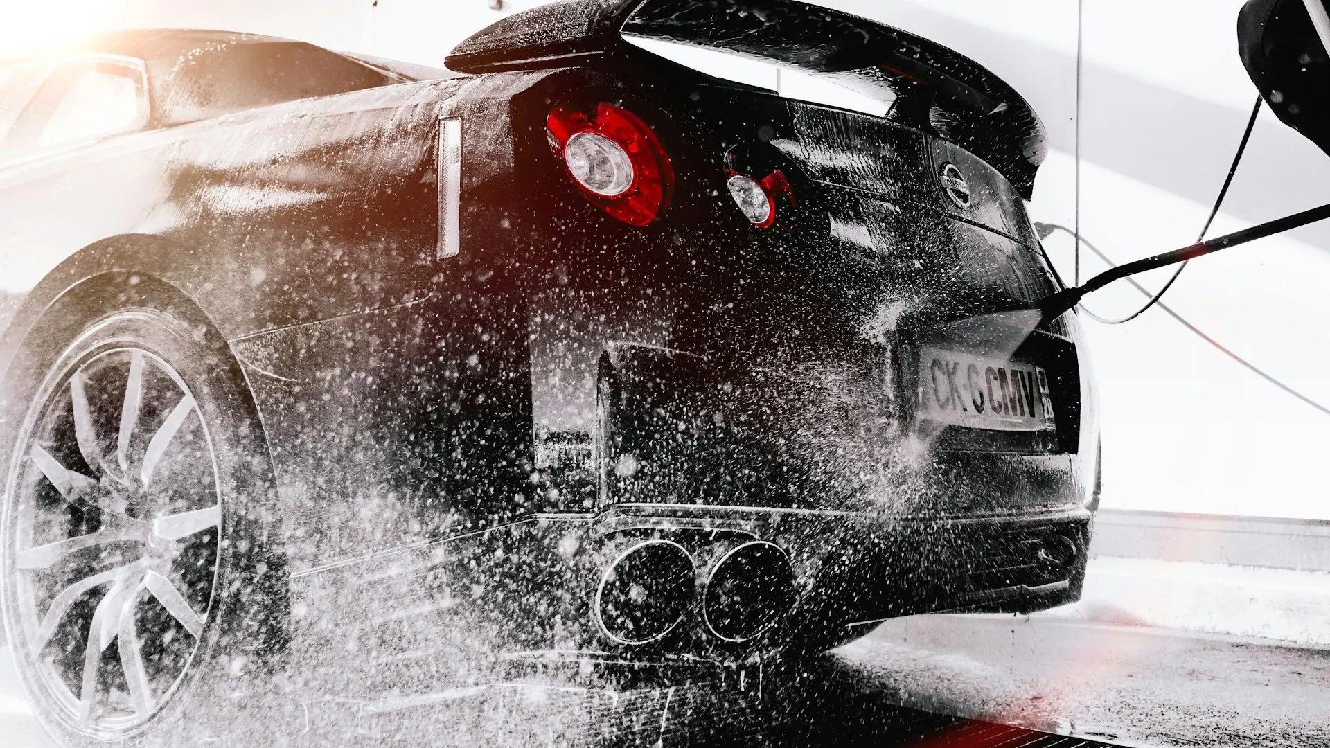 Black sports car being pressure washed during a professional detailing session