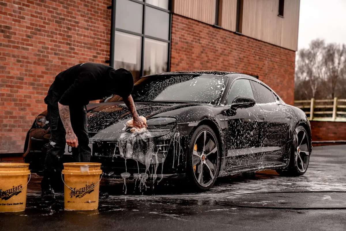 Detailer hand washing a black sports car covered in thick foam